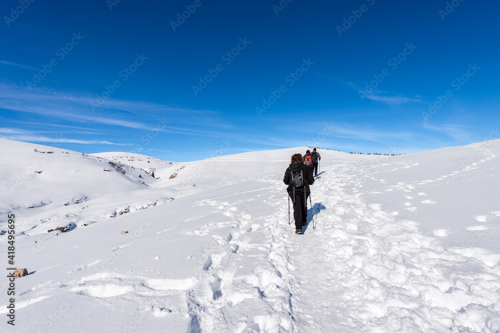 Three Hikers on a snowy footpath in winter landscape on the Lessinia Plateau (Altopiano della Lessinia), Regional Natural Park near Malga San Giorgio ski resort, Verona province, Veneto, Italy, Europe
