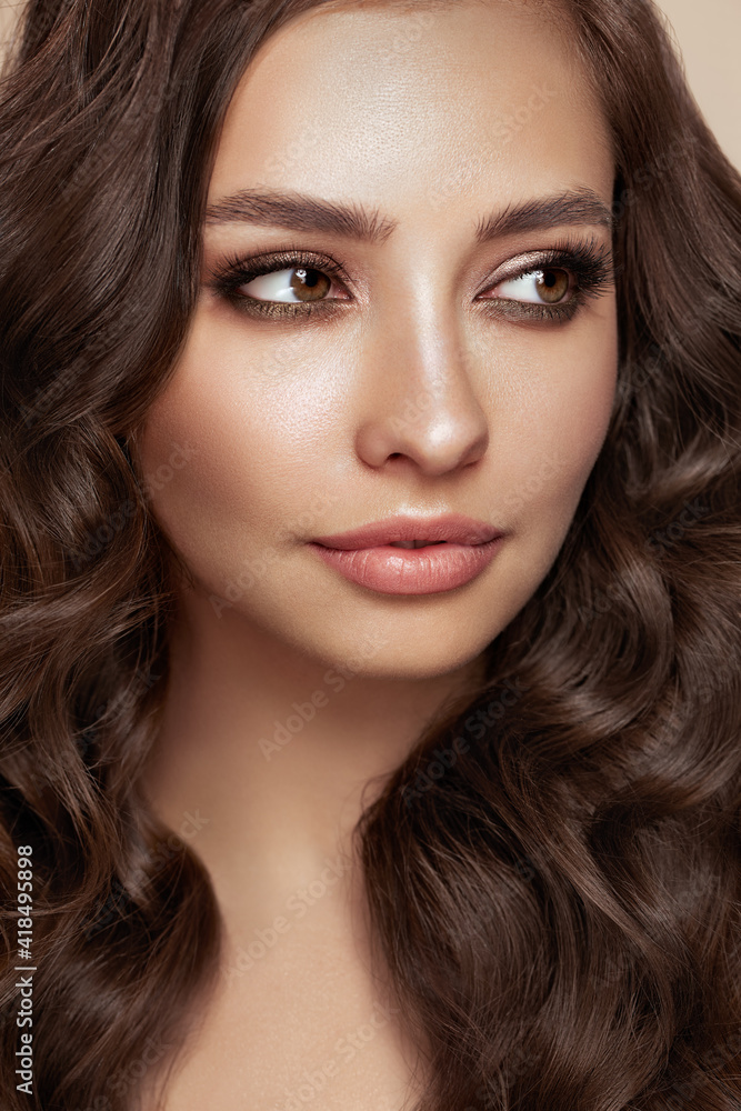 Fototapeta premium Brunette girl with perfect makeup. Smiling beautiful model woman with long curly hairstyle. Care and beauty hair products.