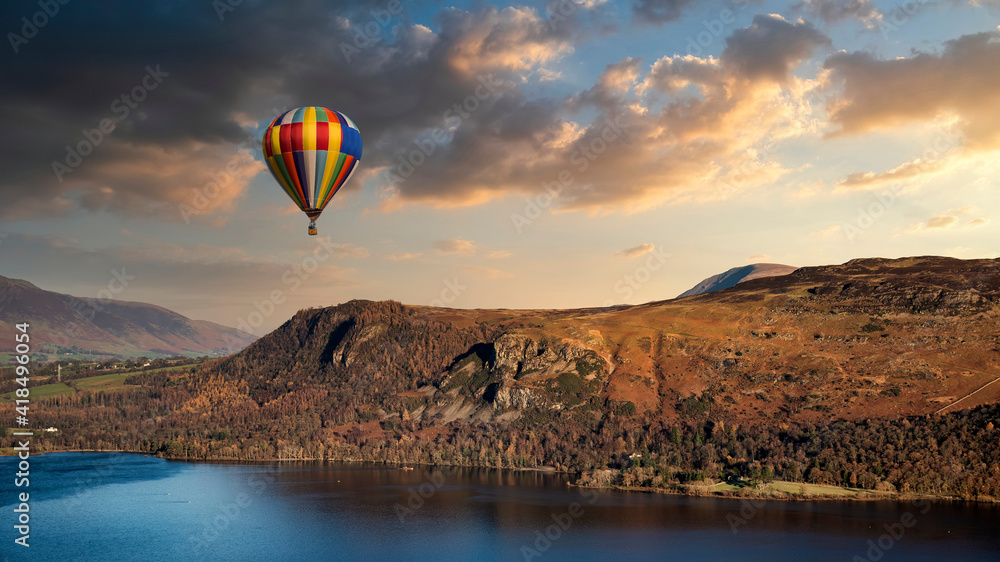 Hot air balloon flying over stunning Derwentwater landscape in Lake District during Summer dunset