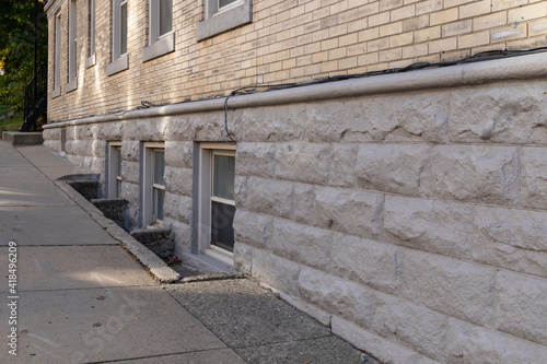 Basement window wells on a building made from rusticated stone and bricks alongside a sloping sidewalk, horizontal aspect photo