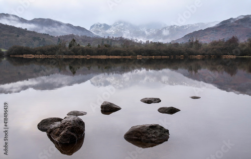 Dramatic landscape image looking across River Brathay in Lake District towards Langdale Piks mountain range on mistry Winter morning photo