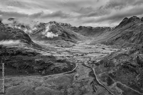 Stunning flying drone black and white landscape image of Langdale pikes and valley in Winter with dramatic low level clouds and mist swirling around