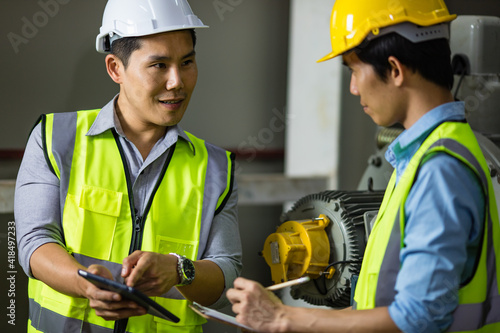 Senior and junior engineers talking together with intimated manner beside the machine in factory. Concept for good teamwork and unity of colleauges photo