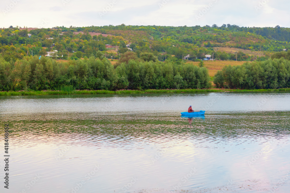 Man fishing from the boat . Blue wooden boat on the river water Man fishing from the boat . Blue wooden boat on the river water