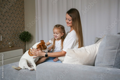 Young mom with her daughter playing with Jack Russell Terrier dog. Family and pet at home. © Valeriya