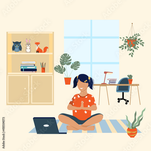 Little girl doing yoga at home using a laptop. Concept for learning at home, yoga school online. Place for text
