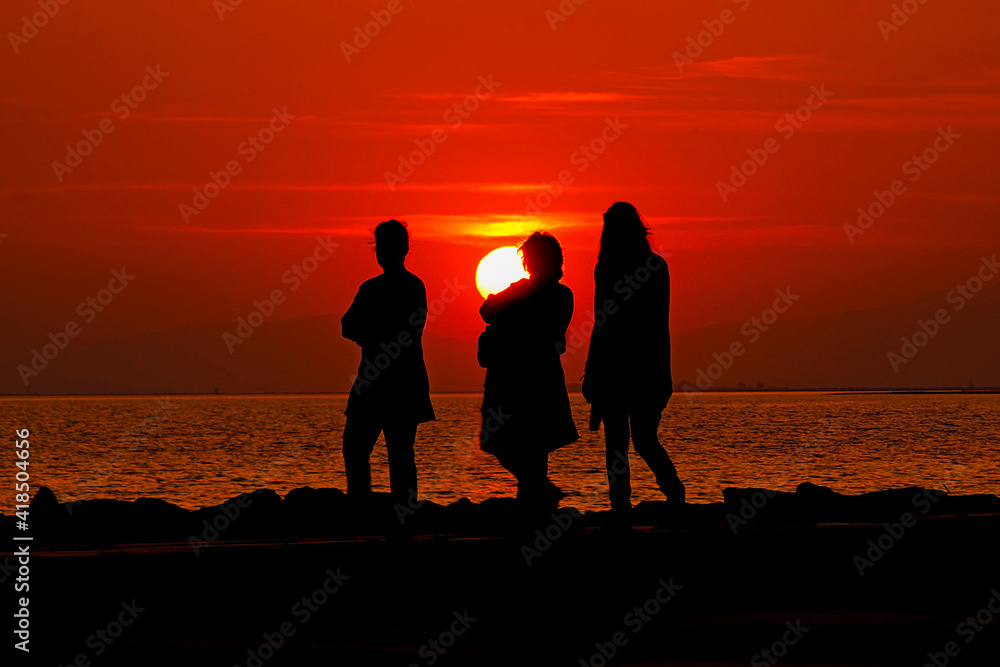 People strolling by the sea at sunset. Silhouettes.