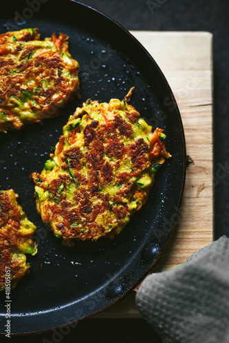 Vegetable zucchini and carrot fritters on a frying pan and a wooden cutting board, close-up top view photo