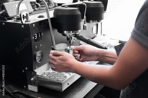 Closed up of barista’s hand holding pitcher full of milk frothing from coffee machine. For making cappuccino or latte. 