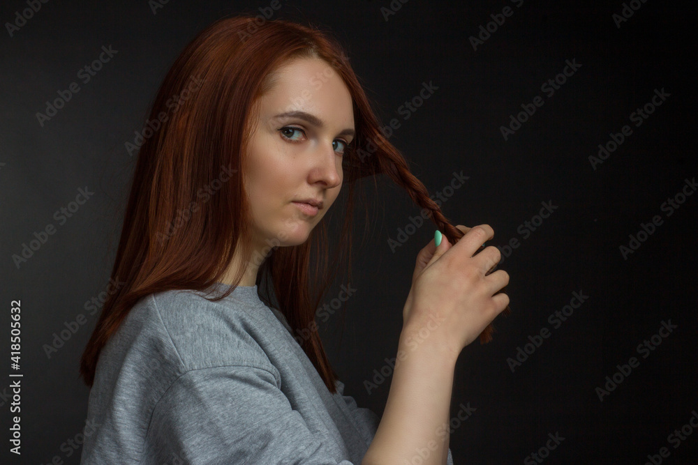 Fototapeta premium Red-haired young girl on black background in a gray T-shirt