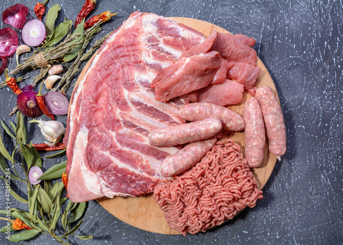 Raw meat products.Barbecue pork ribs, steaks, grilled sausages,minced meat, garnished with spices on a round wooden chopping board.Flat layout.Selective focus.