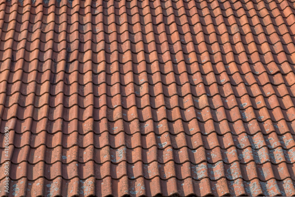 A fragment of an old tiled roof made up of brown shingle elements arranged in wavy rows with traces left by time and precipitation. Natural vintage architectural background. A fragment of an old tiled roof made up of brown shingle elements arranged in wavy rows with traces left by time and precipitation. Natural vintage architectural background.