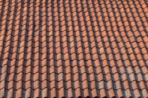 A fragment of an old tiled roof made up of brown shingle elements arranged in wavy rows with traces left by time and precipitation. Natural vintage architectural background.