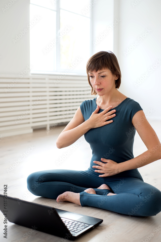 Woman in sportswear sits in front of a laptop and shows exercises Woman in sportswear sits in front of a laptop and shows exercises