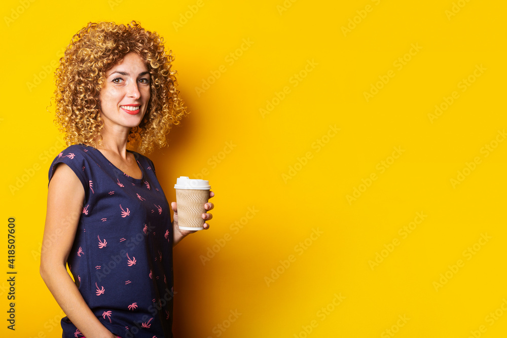 smiling young woman with curly hair holding paper cup on yellow background. smiling young woman with curly hair holding paper cup on yellow background.