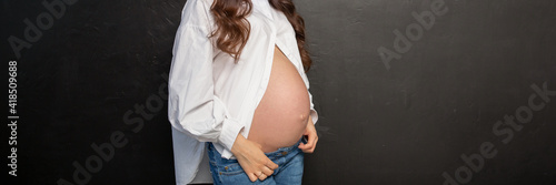 Pregnant woman with long hair, jeans, unbuttoned white blouse on a black background