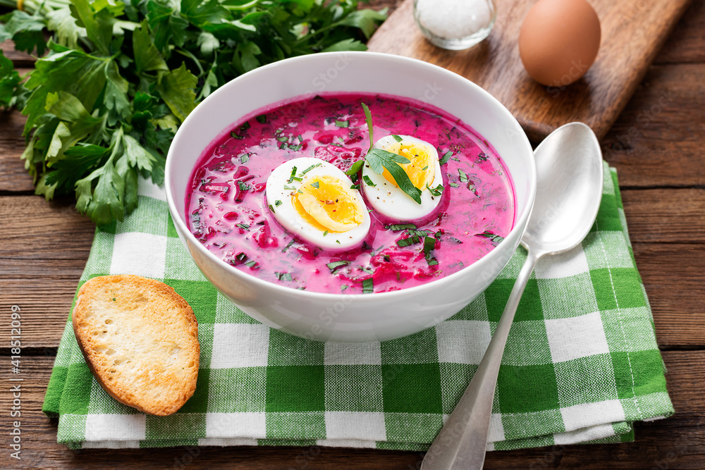 Traditional cold summer beetroot soup with vegetables and boiled egg in a white bowl on wooden table. Traditional cold summer beetroot soup with vegetables and boiled egg in a white bowl on wooden table.