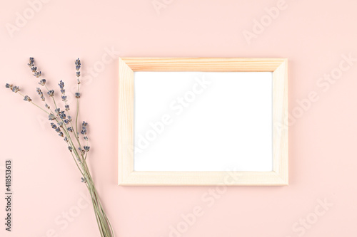 Wooden photo frame with white blank card and flowers on pastel pink background. Mock up poster frame. Stylish template