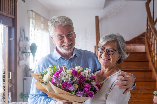 Portrait of couple of two happy and in love seniors or mature and old people holding flowers at home looking at the camera. Pensioners adult enjoying and celebrating holiday together. © Daniel