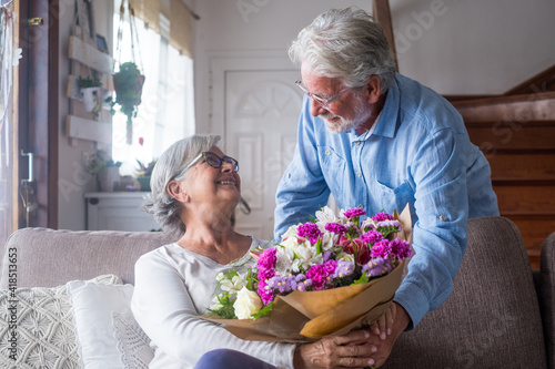Old man giving flowers at his wife sitting on the sofa at home for the San Valentines’ day. Pensioners enjoying surprise together. In love people having fun. © Daniel