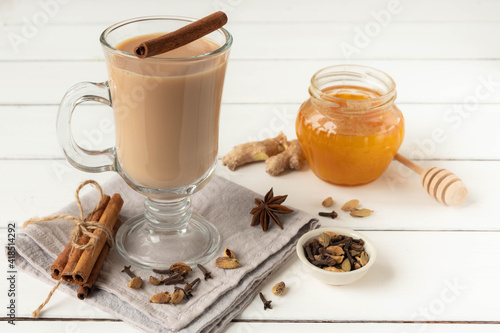 A glass of hot Indian masala tea brewed with aromatic spices, honey and milk. White wooden background, copy space