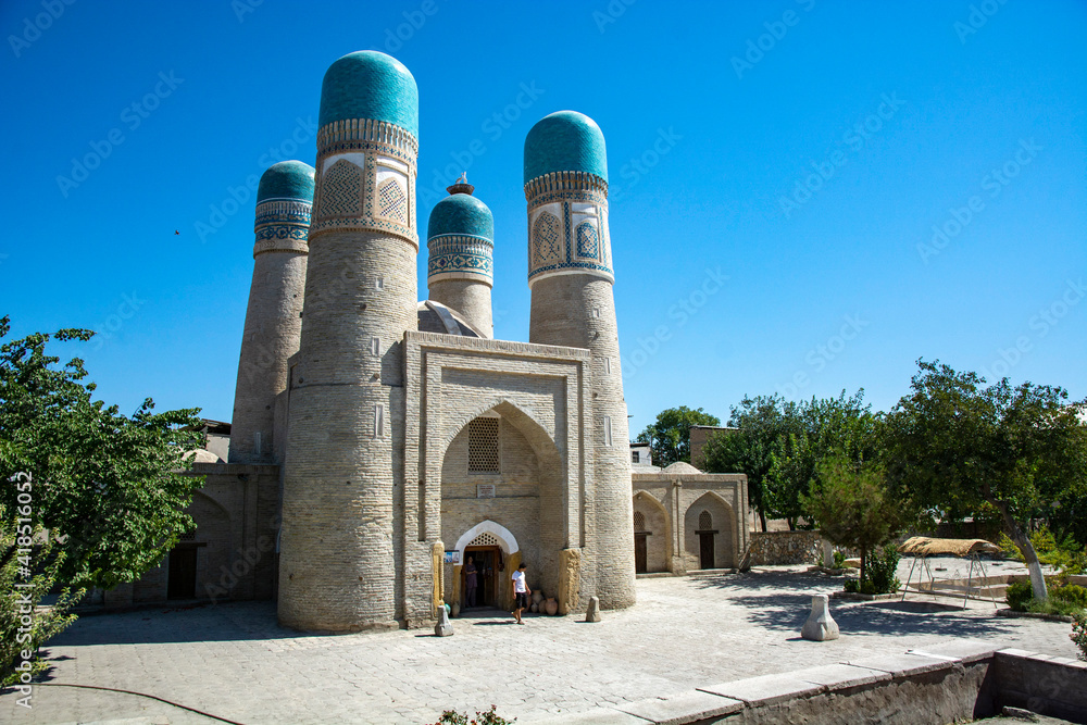 uniq looking mosque with four towers in living blocks of Buchara with bushes and no-one around 