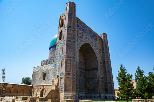 mosque with huge entrance madrasah in hot day light with wall and trees 