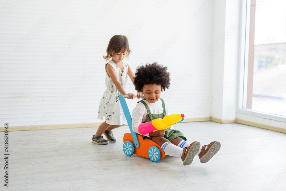.A white child and a black child playing a stroller, black looks, smiling at the camera. Concept Non-racism. .A white child and a black child playing a stroller, black looks, smiling at the camera. Concept Non-racism.