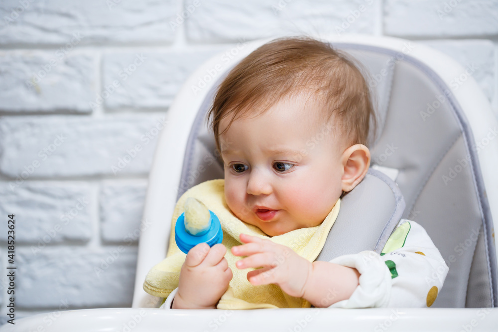 A small child sits on a high chair and eats fruits through the net. Nibbler for feeding babies A small child sits on a high chair and eats fruits through the net. Nibbler for feeding babies