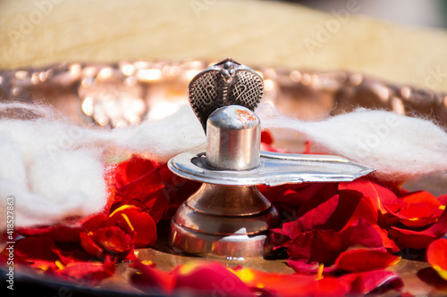 Stock photo of a silver shivlinga which is icon of lord shiva snake above shivlinga, being worshiped flowers and cotton garland on occasion of Indian festival mahashivratri or shivratri photo