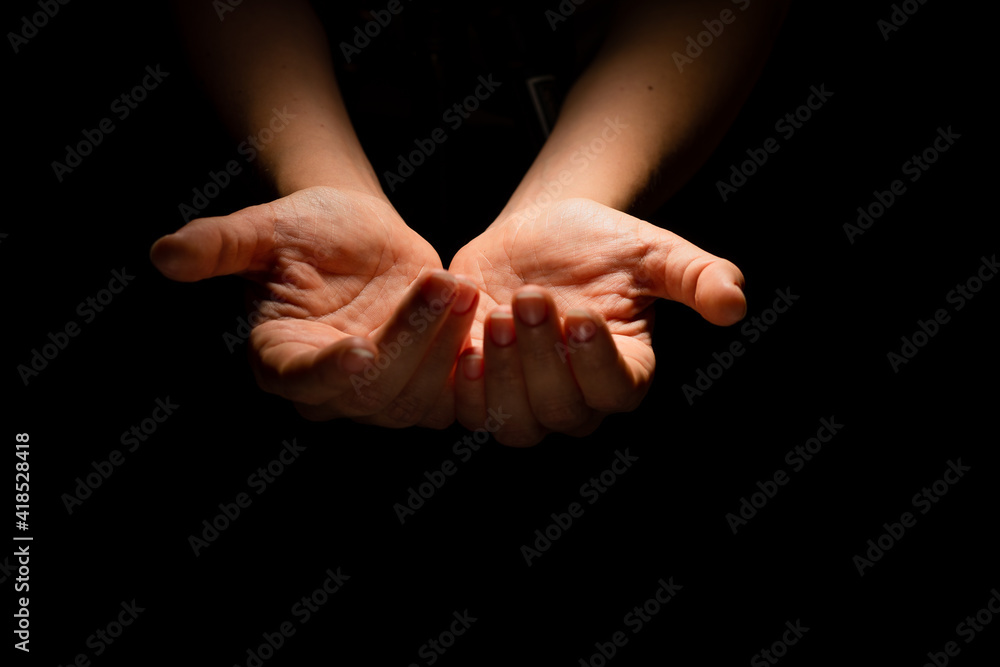 Two hands with open palms turned up, offering or giving something, a handful. Hands on a black background, contrasting dramatic light from above