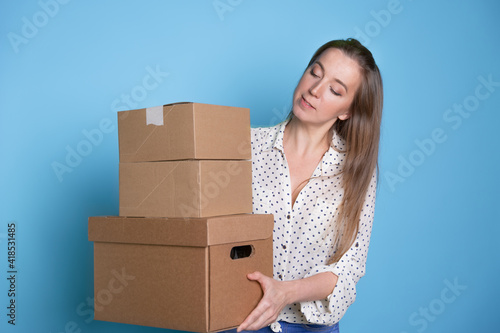 Accept a parcel, happy young woman holding a stack of cardboard boxes, portrait on a blue background