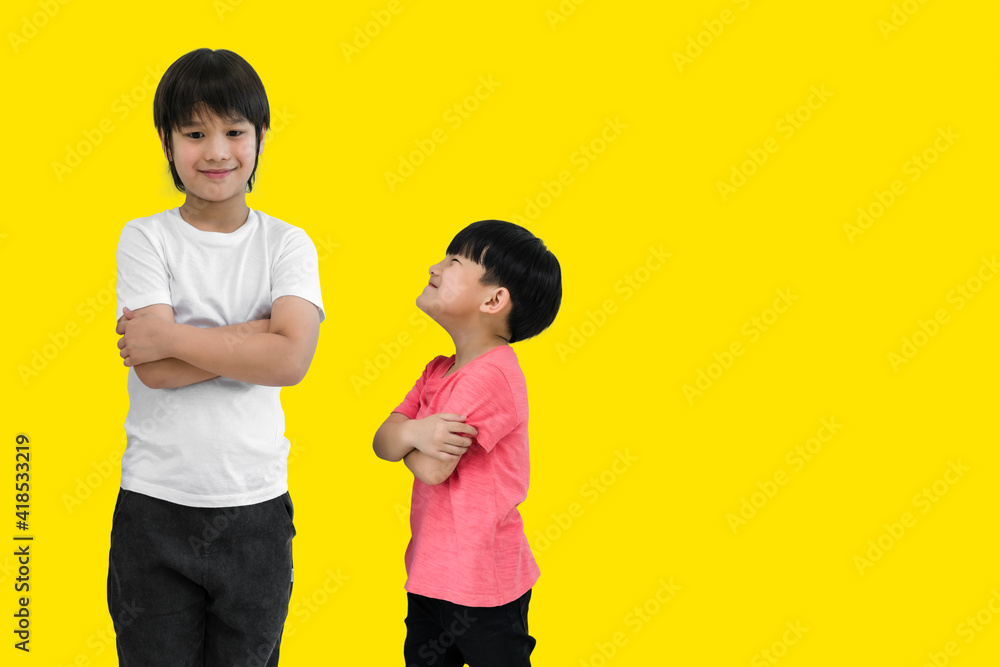 Little child boy and tall child boy standing arms crossed and looking face isolated on yellow background. Big and small kid concept at be friends. Back to school for concept. Little child boy and tall child boy standing arms crossed and looking face isolated on yellow background. Big and small kid concept at be friends. Back to school for concept.