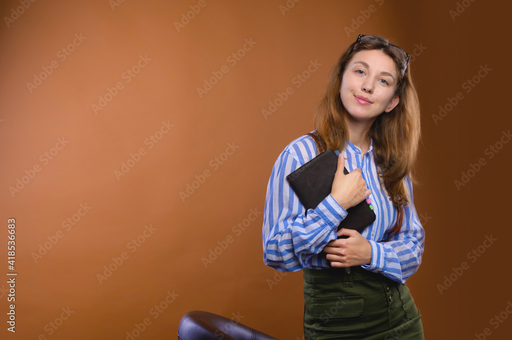 Obraz premium Portrait of a friendly positive Caucasian young woman dressed in corporate formal dress with a notepad in her hands. Smiling looks into the camera. Studio portrait