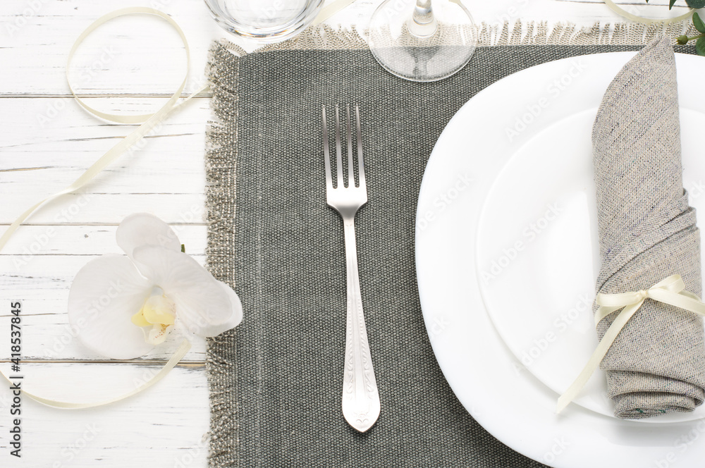 Romantic table setting with orchid and gray napkin on white wood background