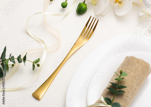 Wedding table setting with white crockery, gold cutlery and flowers on a white tablecloth, holiday table setting