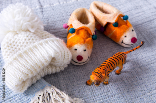Flat lay still life with childhood objects including a tiger toy, a wooly hat and felt slippers on cozy pale blue fringed throw blanket