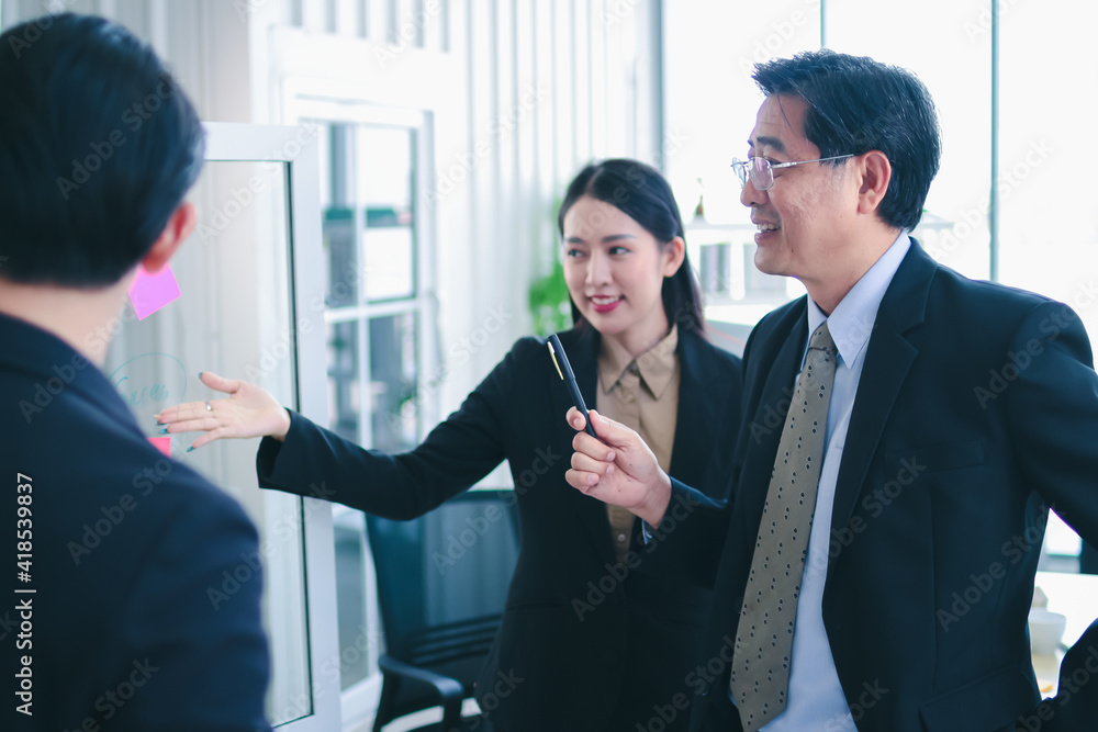 asia business man and woman pointing to paper post it on glass board explain document with manager in the office.businesswoman in meeting with colleagues, gesturing.Selective Focus asia business man and woman pointing to paper post it on glass board explain document with manager in the office.businesswoman in meeting with colleagues, gesturing.Selective Focus