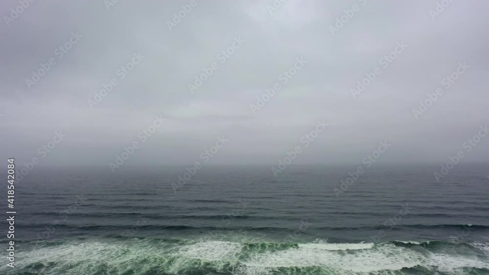 Aerial shot of waves splashing in sea against cloudy sky, drone flying forward towards horizon - Cannon Beach, Oregon