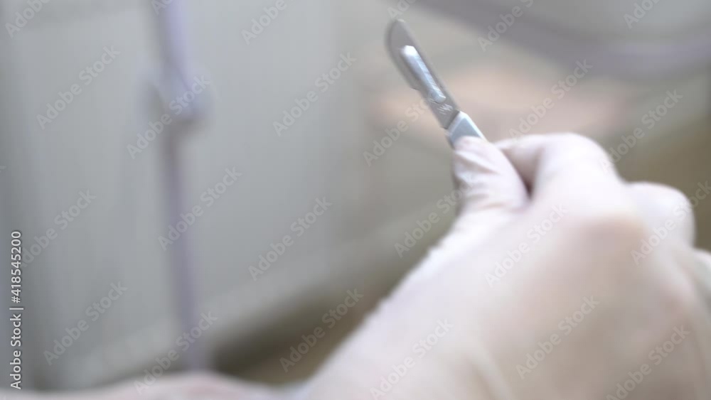 A woman with white gloves installing a scalpel blade to a handle. Medical scalpel in doctor's hands isolated on white blurred background. Hand of surgeon in white medical glove holding a scalpel. A woman with white gloves installing a scalpel blade to a handle. Medical scalpel in doctor's hands isolated on white blurred background. Hand of surgeon in white medical glove holding a scalpel.