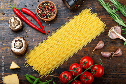 Raw pasta with fresh tomatoes, peppers, asparagus beans, spices and cheese on a wooden table.