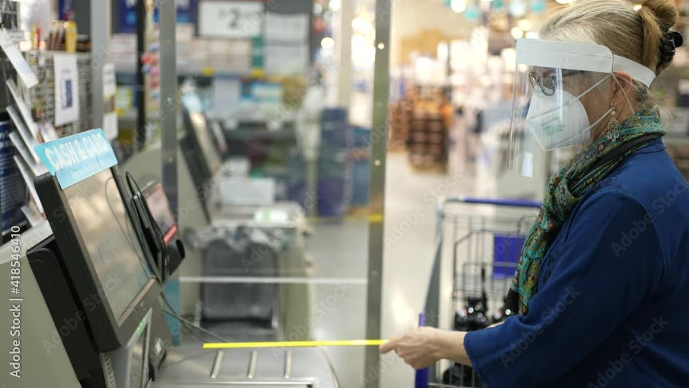 Mature woman wearing face shield and mask at the self checkout in a big box retail hardware store. Concept of safe shopping during pandemic. Mature woman wearing face shield and mask at the self checkout in a big box retail hardware store. Concept of safe shopping during pandemic.