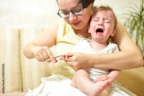 selective focus The mother cuts the child's toenails on the arm with baby safe scissors. Self care authentic concept. Mother care is most important for baby healthy life lifestyle. The baby is crying