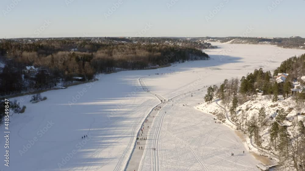 Ice skating in nature from above in drone video. Frozen lake pond or fjord river with track for skaters on frozen surface. tilting beautiful high angle aerial overview. Ice skating in nature from above in drone video. Frozen lake pond or fjord river with track for skaters on frozen surface. tilting beautiful high angle aerial overview.