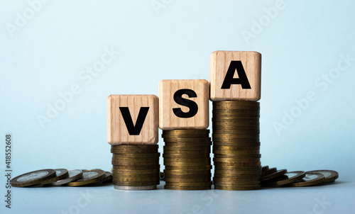 VSA - acronym on wooden cubes. Which stand on stacks of coins on a light background