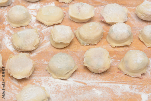 Homemade dumplings with meat on wooden table with flour. Ravioli for cooking dinner. Close-up, selective focus