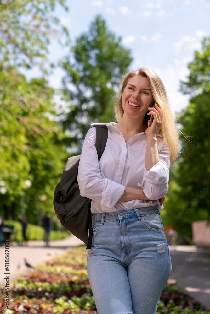 a girl with a backpack walks in the park on a sunny day and smiles while talking on a mobile phone a girl with a backpack walks in the park on a sunny day and smiles while talking on a mobile phone
