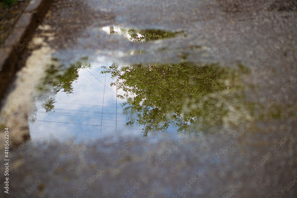 Blue sky and green trees reflection in spring puddle Blue sky and green trees reflection in spring puddle