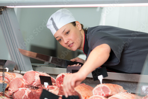 female butcher holding knife reaching across meat counter