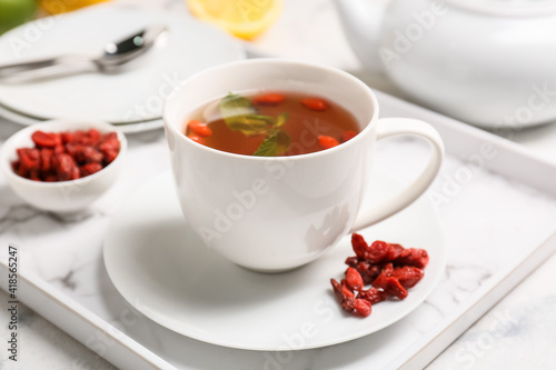 Cup with goji tea on light background